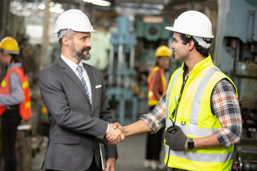Recruitment consultant and construction company executive shaking hands after a successful hiring process while newly recruited construction professionals prepare to begin work on an active UK building site